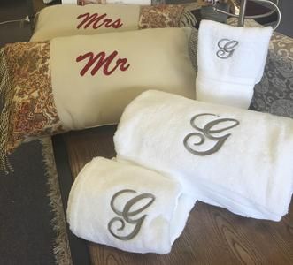 Embroidered pillows and towels with initials and titles on a wooden table.